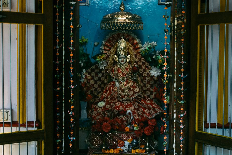 Colourful statue of Indian traditional god sculpture on throne with bright clothes decorated with flowers in traditional oriental altar for home prays and meditations